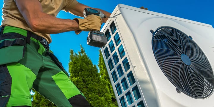 worker holding a drill to install a heat pump outside 