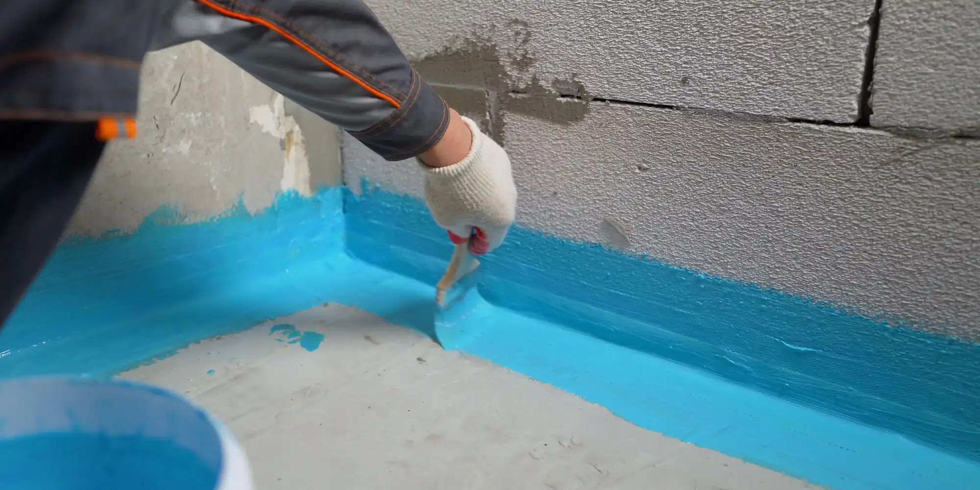 person using a blue coloured sealant in a basement to waterproof the floor.