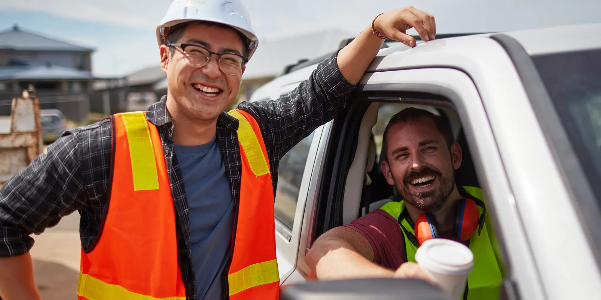 two contractors smiling, one sitting in truck holding coffee while the other is outside the truck